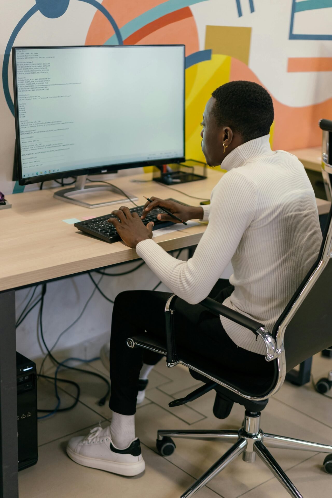 Young man coding at computer in a stylish office environment, focused and working efficiently.